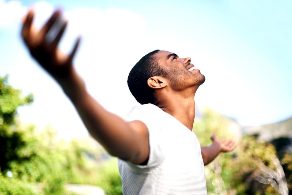 A young man looking upwards with arms wide open.